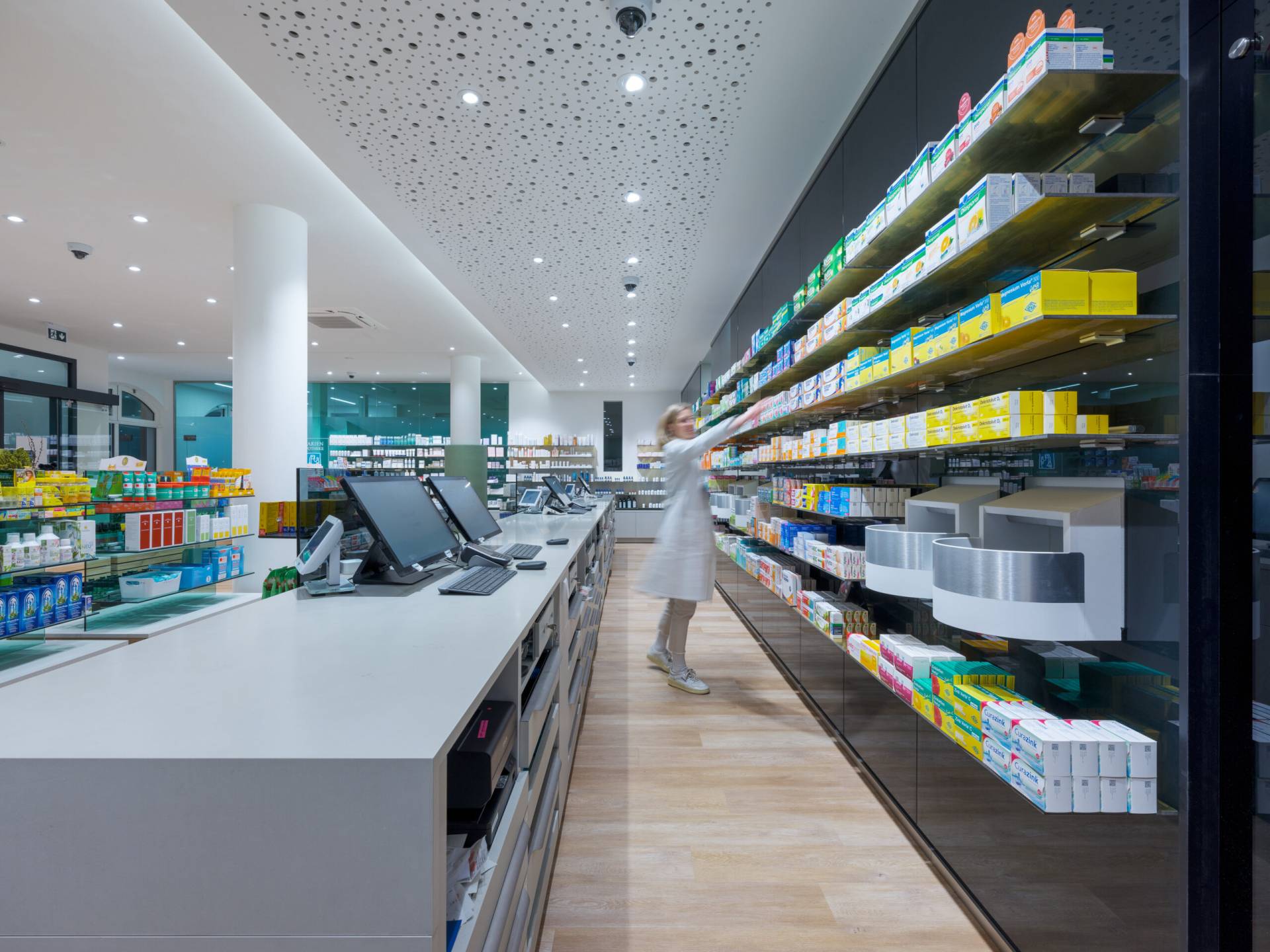 Marien-Apotheke in Moosburg, Innenarchitektur / Interior Design von Planquelle, Offizin und Regale mit Waren und Apothekerin beim Einräumen
