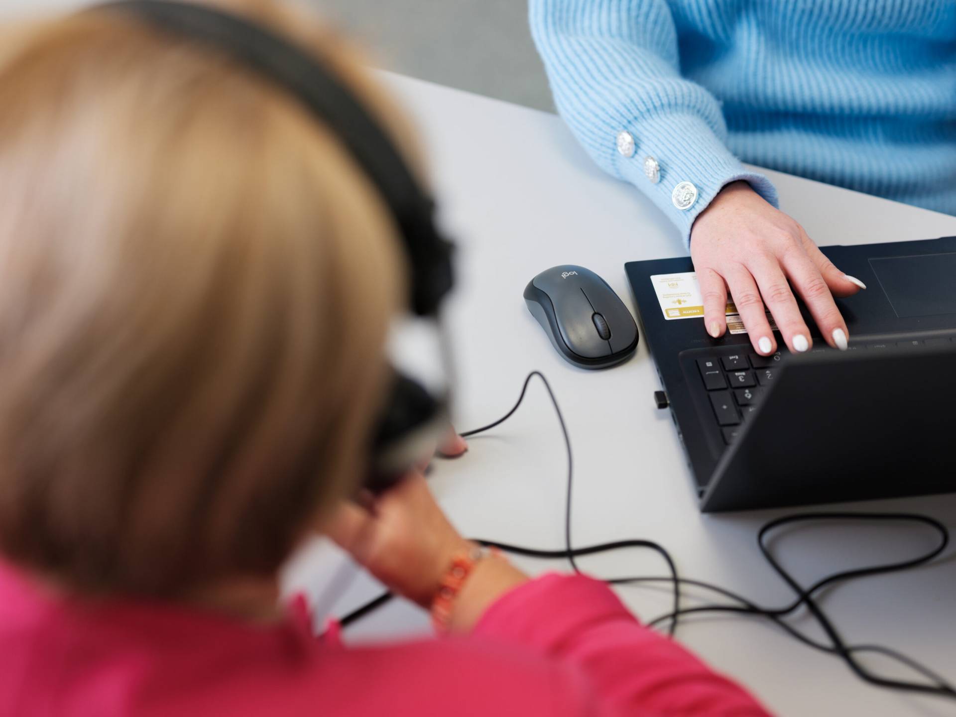 Blick von oben auf Laptop und Hand einer Hörgeräteakustikerin welche die Hörfähigkeit ihrer Kundin prüft