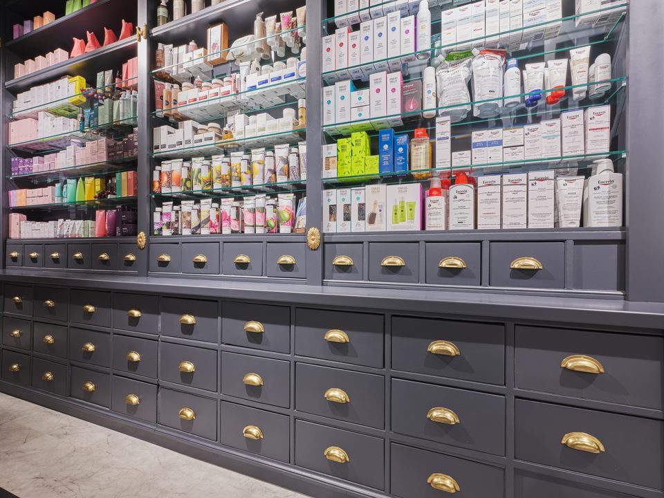 Schubladenwand aus mattschwarzem Holz mit goldenen Muschelgriffen in der Apotheke Schwarzer Adler in Wien, darüber Glasböden mit Pflegeprodukten