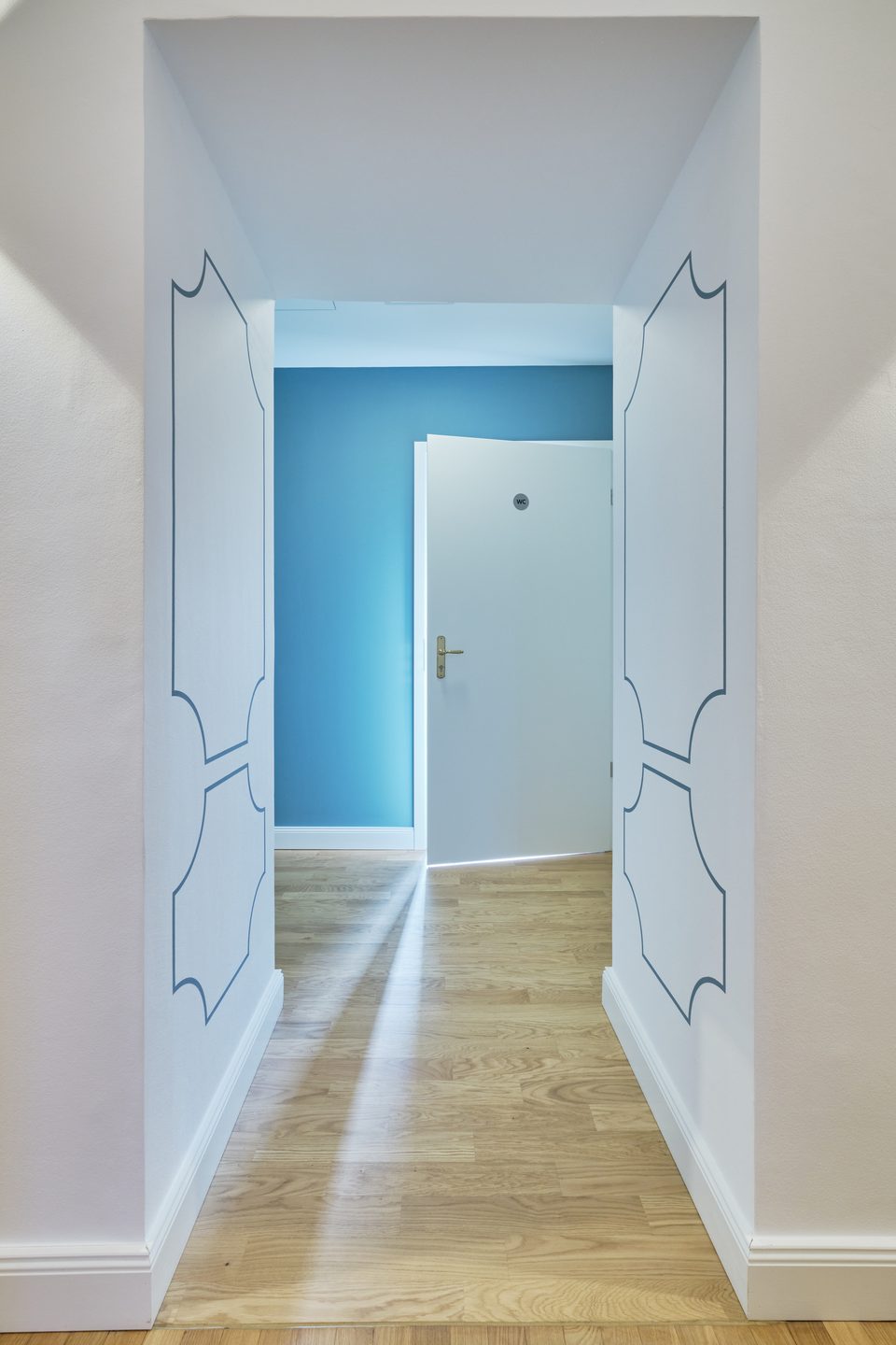 Flur der Augenarztpraxis im Schloss mit ornamental gezeichneten Wandmustern, der in einen türkis gestrichenen Abschnitt führt