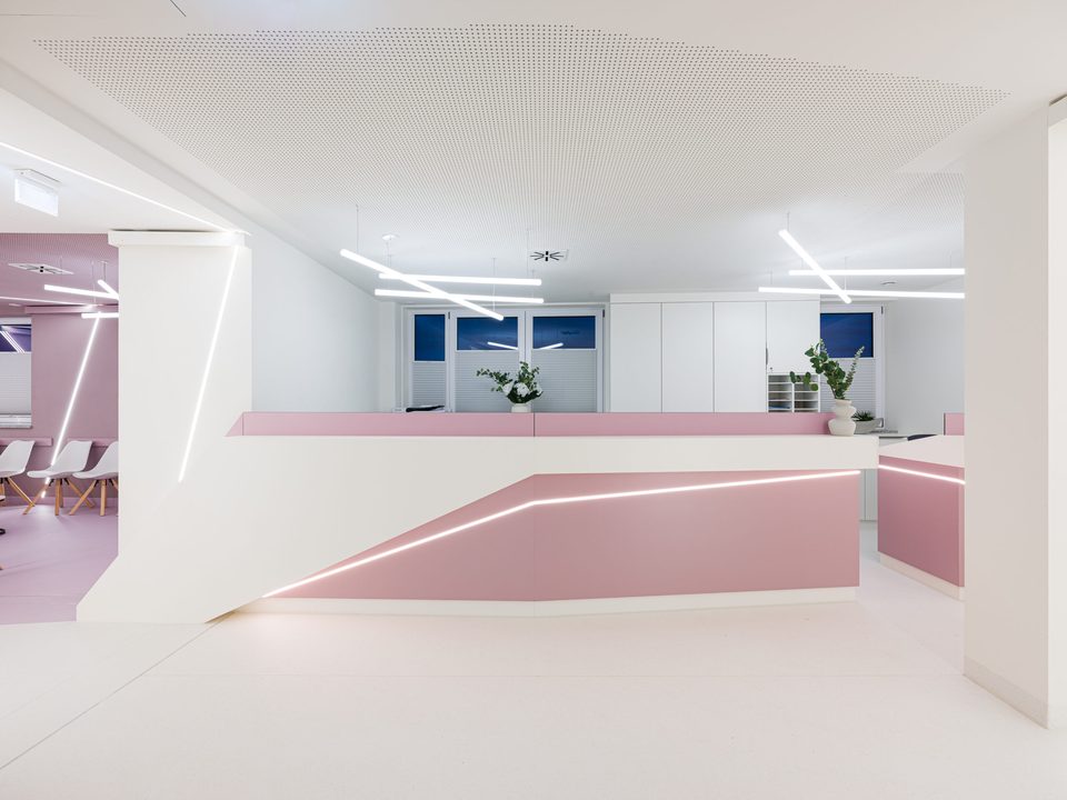 Offener Empfangsbereich mit roséfarbenem Tresen, dahinter die weite Halle mit blauen Fensterflächen