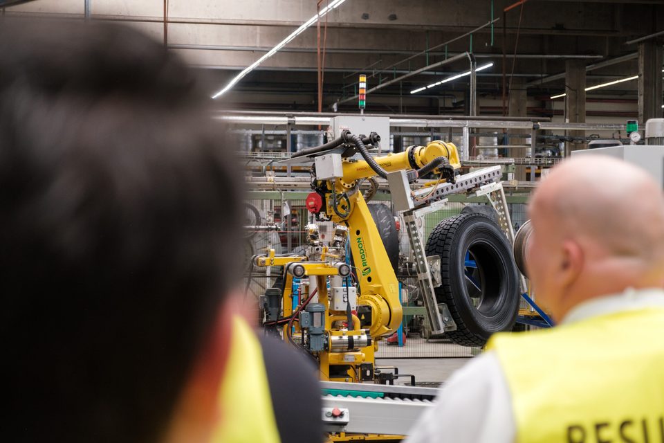 Über die Schulter eines Besuchers fotografiert: der Roboterarm setzt einen Reifen auf die Fördereinrichtung