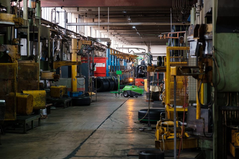 Blick durch die lange Maschinenstraße der Werkshalle, in der Tiefe fährt ein Transportroboter
