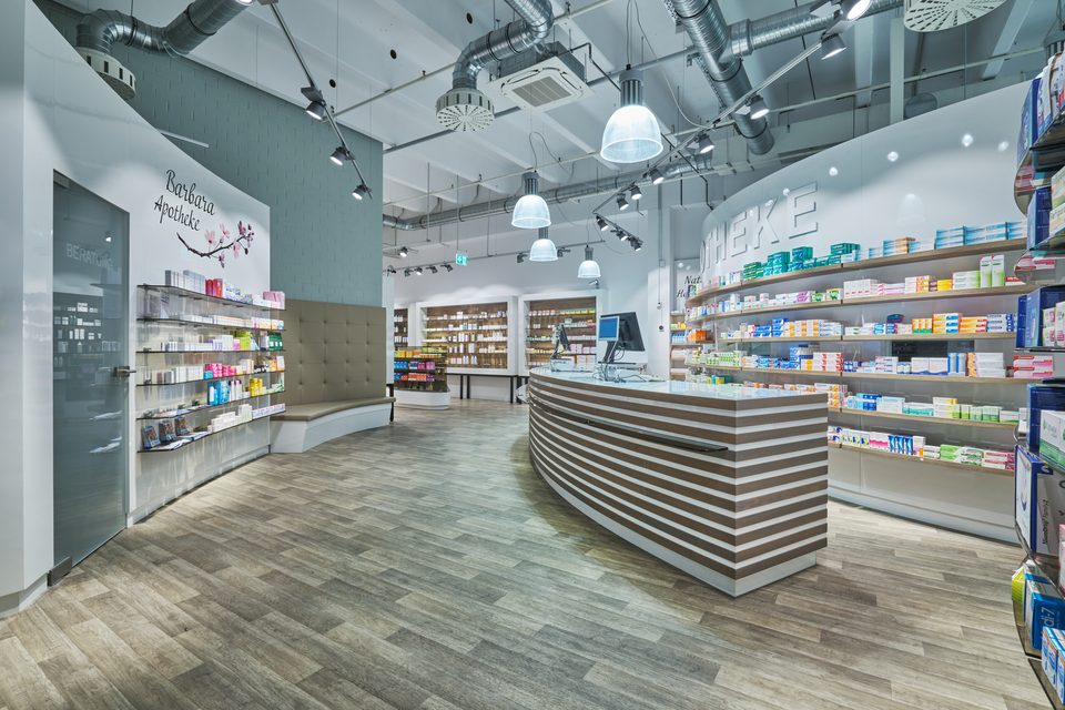 Offizin der Barbara-Apotheke Ingolstadt mit geschwungenem Streifentresen unter großen Industripendelleuchten