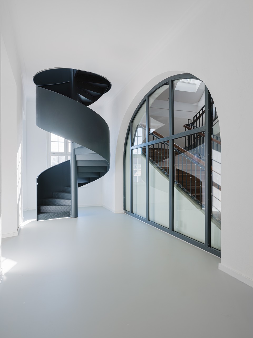 Dunkle Metallwendeltreppe neben Rundbogenverglasung und Holztreppe im Treppenhaus der Bettenhäuser Klinikum Schwabing