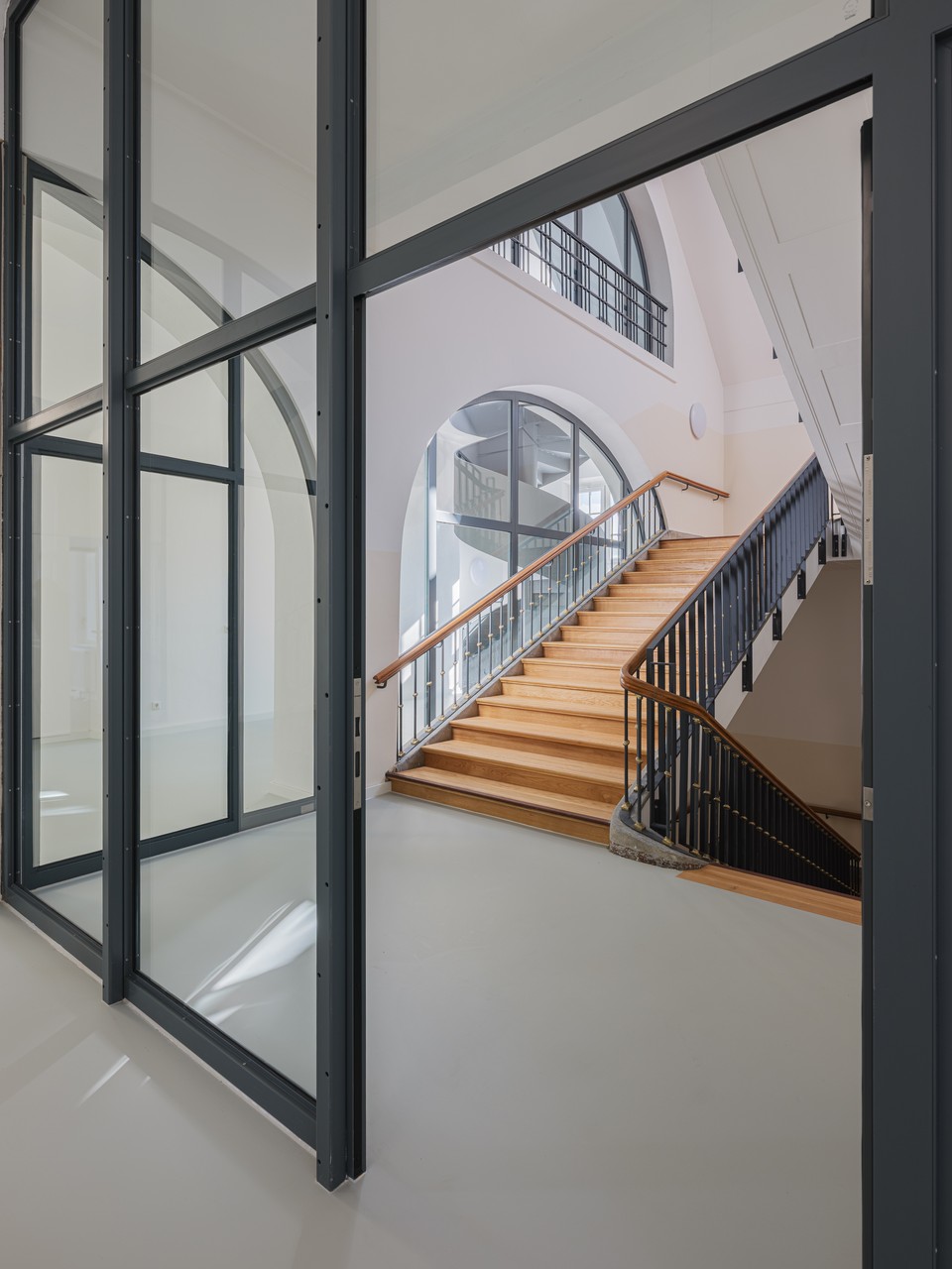 Blick durch anthrazit gerahmte Glaswände auf die Holztreppe mit Metallgeländer im Erschließungskern