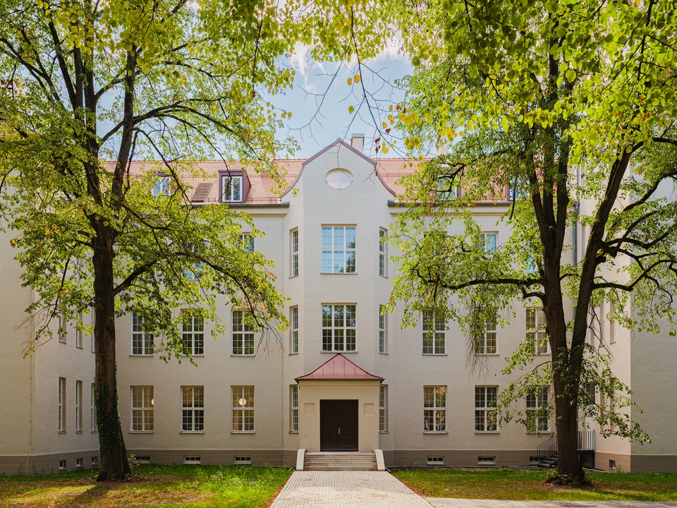 Symmetrische Fassade der Bettenhäuser hinter Bäumen, heller Putz und rotes Ziegeldach