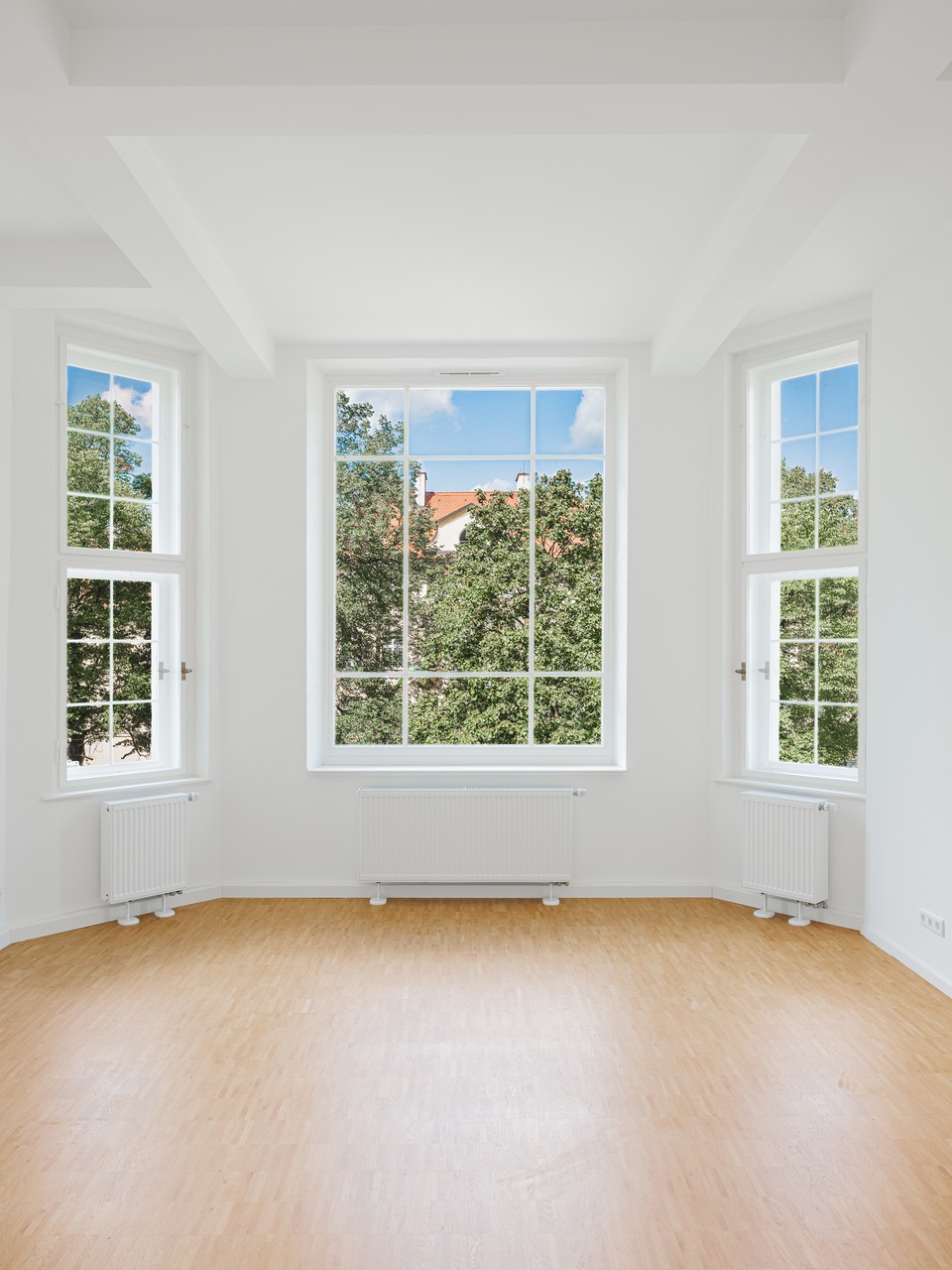 Heller Wohnraum mit Erkerfenstern, Industrieparkett und Blick auf Bäume