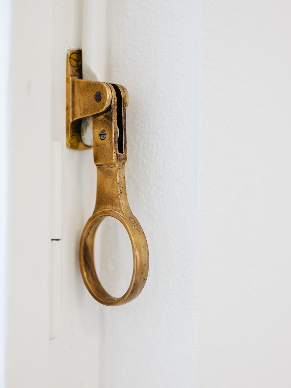 Detail eines historischen Messing-Ringgriffs an weiß lackiertem Holzrahmen