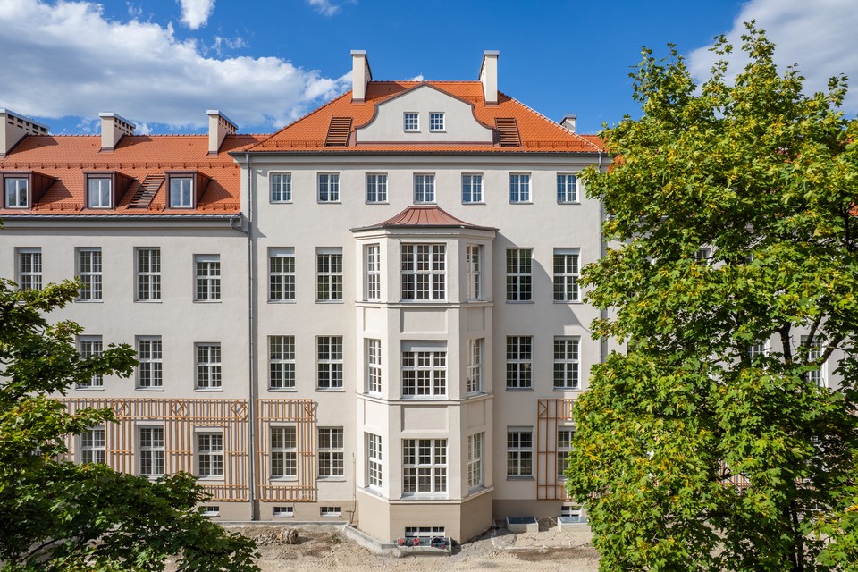 Fassade mit Erker und rotem Ziegeldach, gerahmt von Bäumen