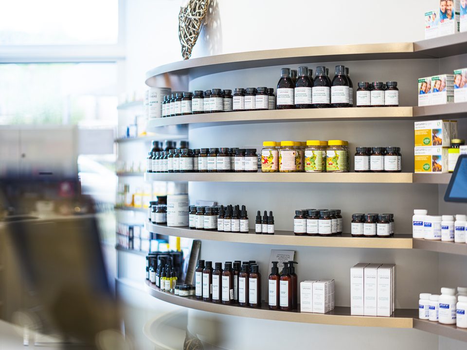 Geschwungenes Regal mit den dunklen Apothekerflaschen der Eigenherstellung, im Vordergrund unscharf die Theke