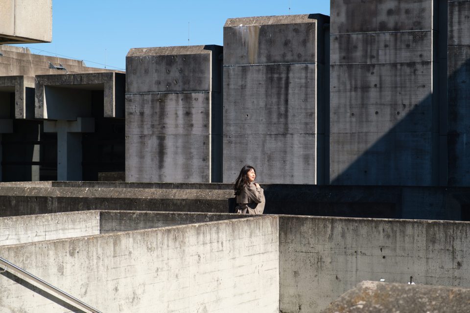 Zwischen den Betonkuben der Universität sitzt eine Besucherin allein auf der Mauer