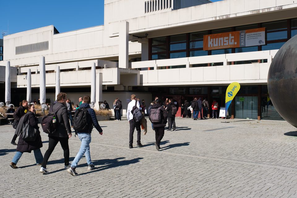 Teilnehmende überqueren den Campusplatz zwischen den Betonbauten der Universität Regensburg