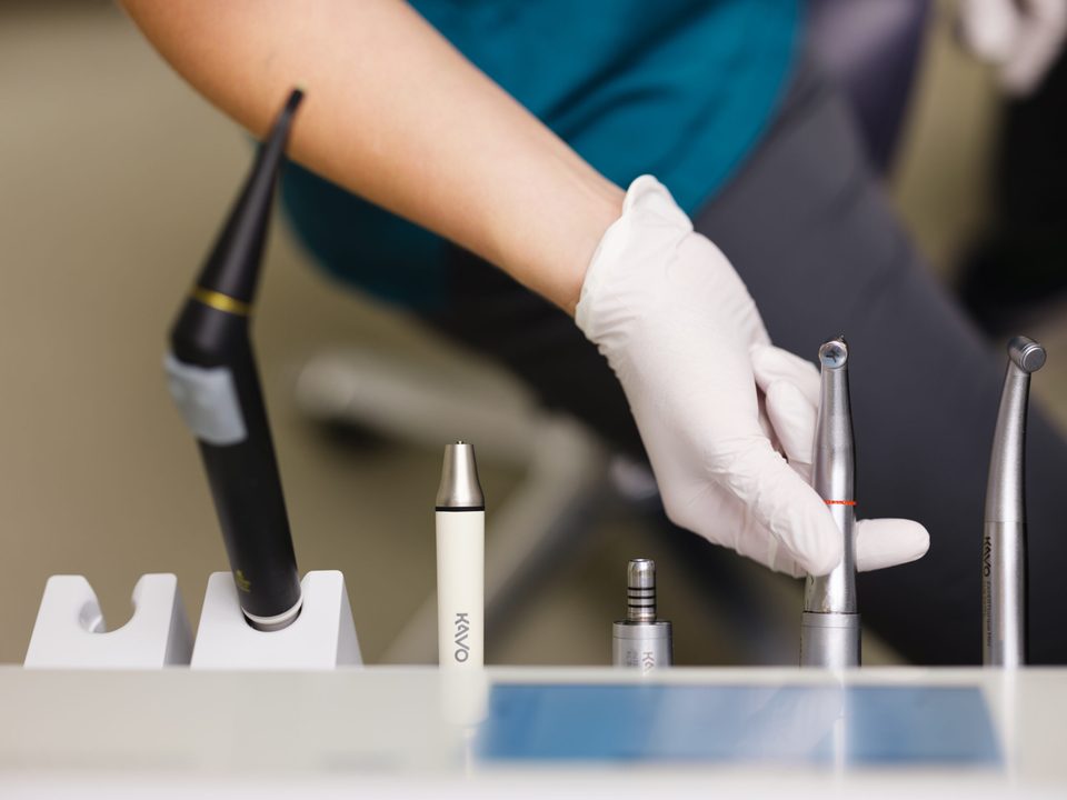Hand mit Handschuh nimmt ein Winkelstück von der Ablage mit vorbereiteten Instrumenten