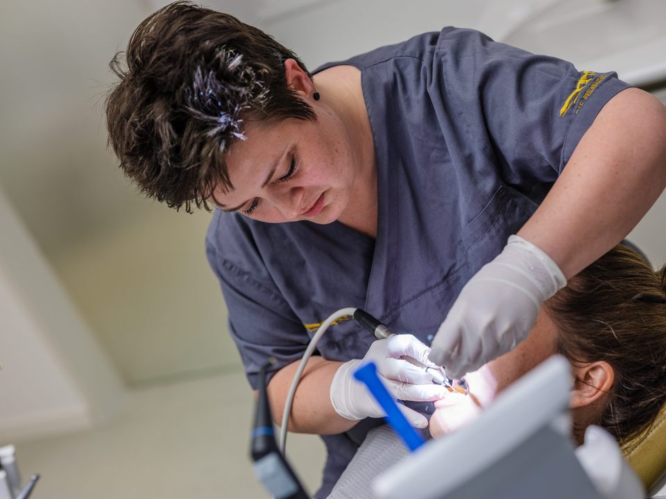 Zahnärztin im grauen Kasack arbeitet konzentriert mit dem Handstück am Patienten