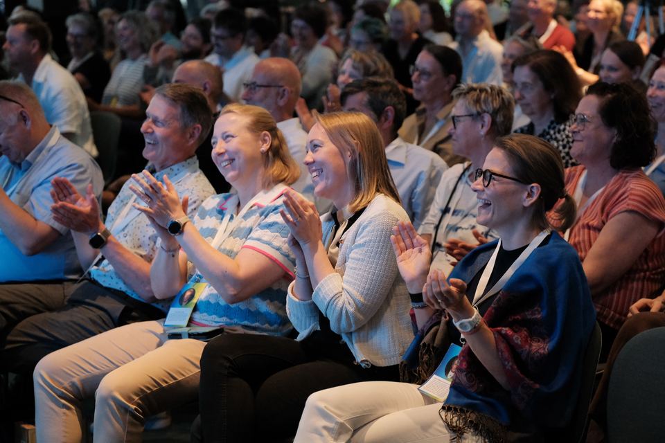 Teilnehmende in den Sitzreihen lachen und applaudieren