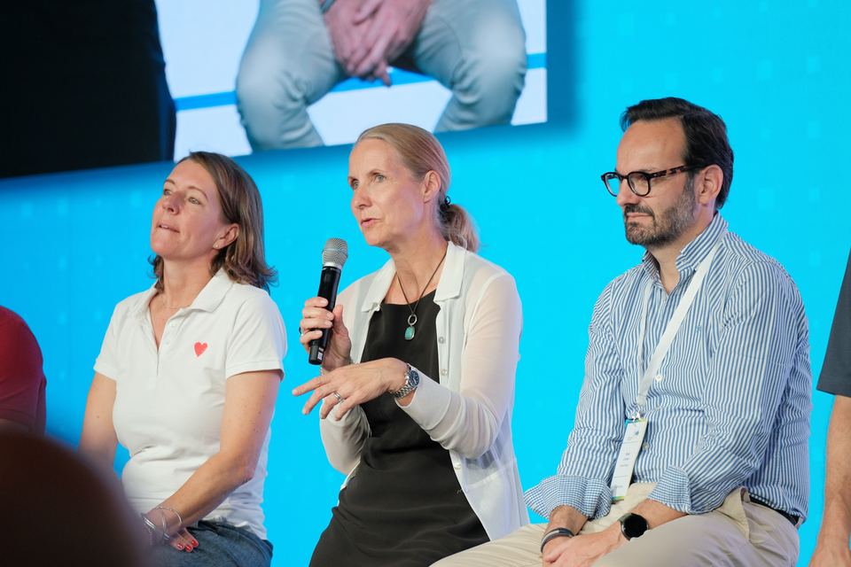 Teilnehmerin der Gesprächsrunde spricht ins Mikrofon, neben ihr hören zwei Personen aufmerksam zu