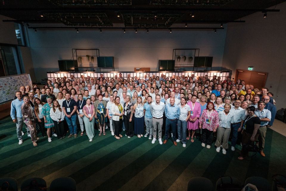 Gruppenbild aller Teilnehmenden, die dicht beieinander im Saal stehen