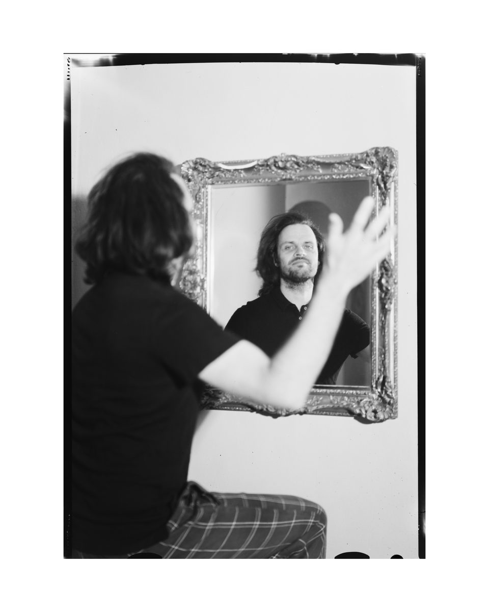 Portrait eines jungen Mannes über eine Spiegelung in einem Spiegel in seinem Haus mit einer Großbildkamera auf Negativfilm