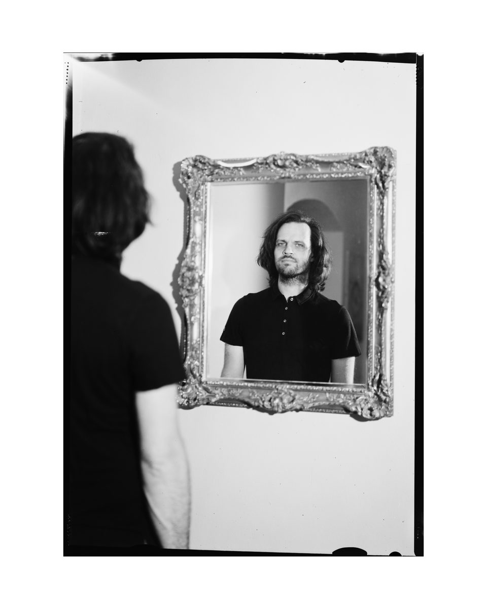 Portrait eines jungen Mannes über eine Spiegelung in einem Spiegel in seinem Haus mit einer Großbildkamera auf Negativfilm