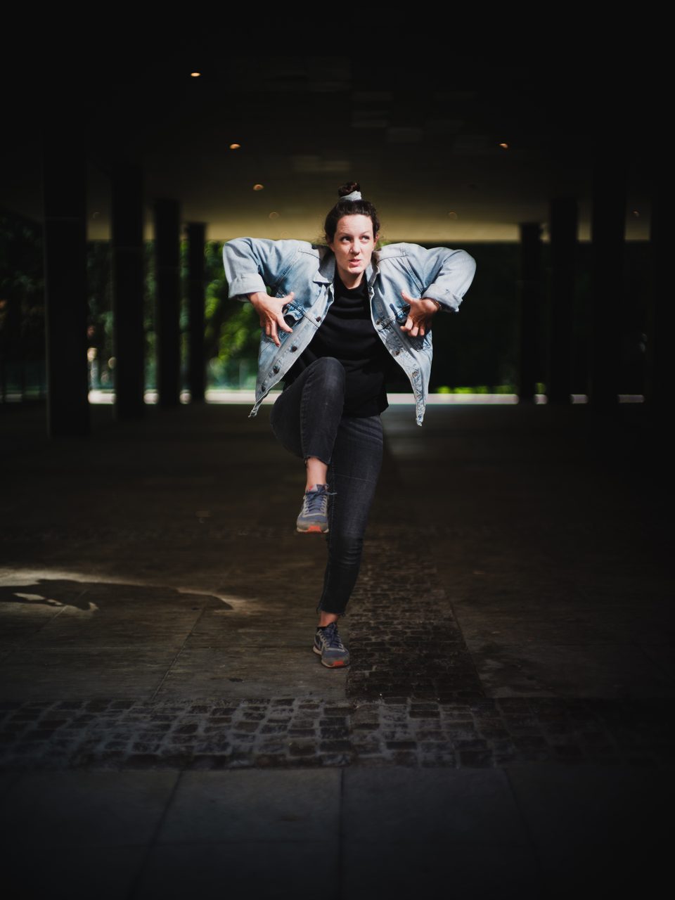 Junge Frau mit ausgefallener Pose im Spotlight unter einem Gebäude
