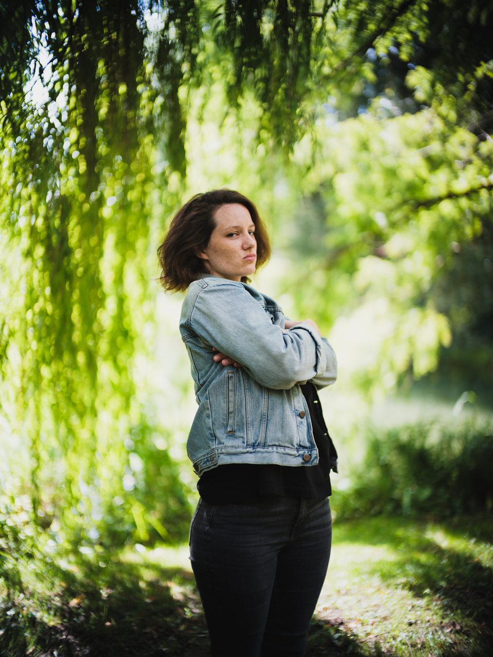 Dreiviertelportrait einer jungen Frau im diffusen Licht und viel Hintergrundunschärfe grünen Laubes im Stadtpark Regensburg