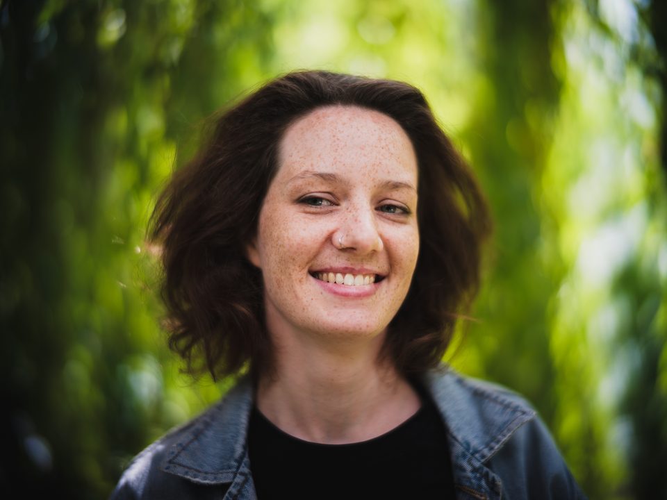 Kopfportrait einer lächelnden, jungen Frau im diffusen Licht im Stadtpark Regensburg