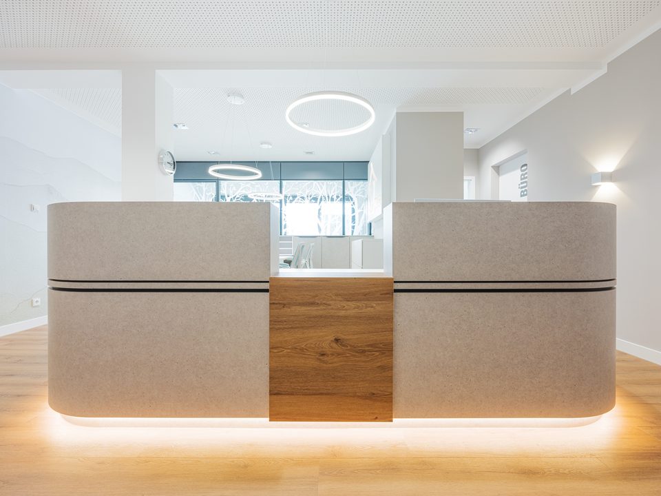 Frontalansicht der Empfangstheke mit Holzmittelstück, Steinoptik und zwei Ringpendelleuchten