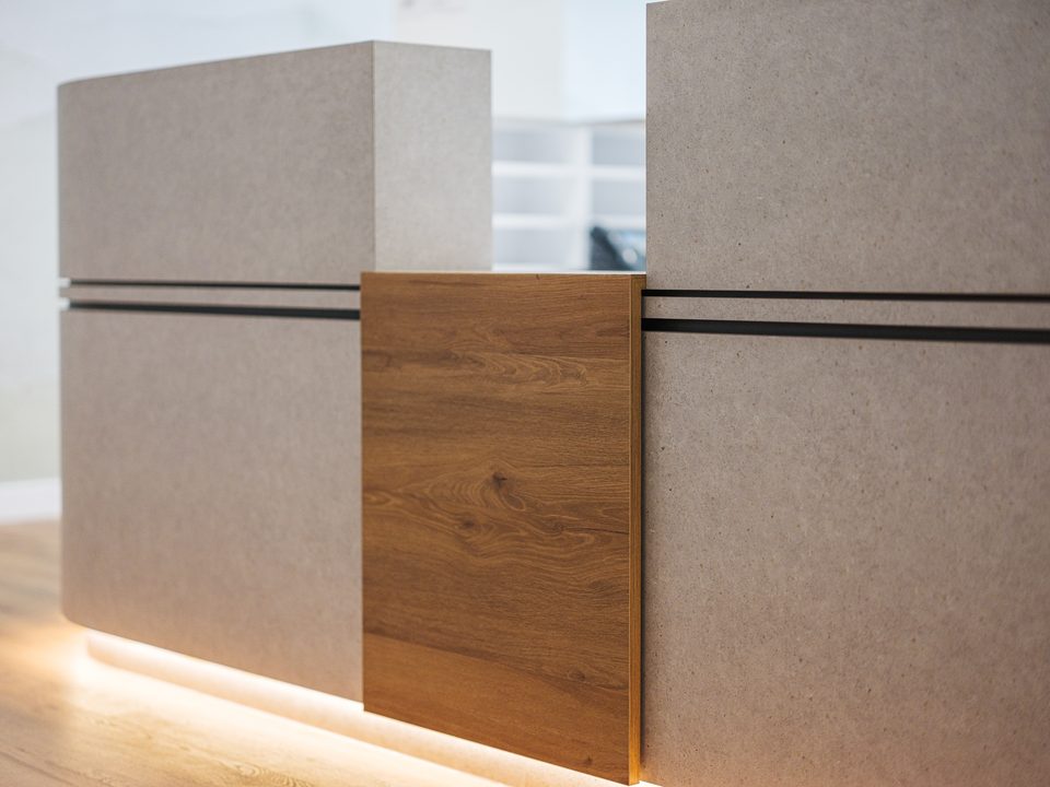 Detail der Empfangstheke: Steinoptik, vertikales Holzpaneel und warmes LED-Licht am Sockel