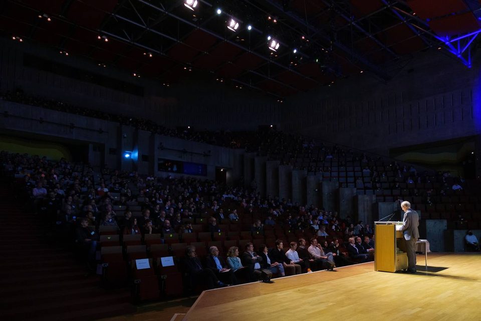 Redner am Pult vor vollem Auditorium einer wissenschaftlichen Konferenz