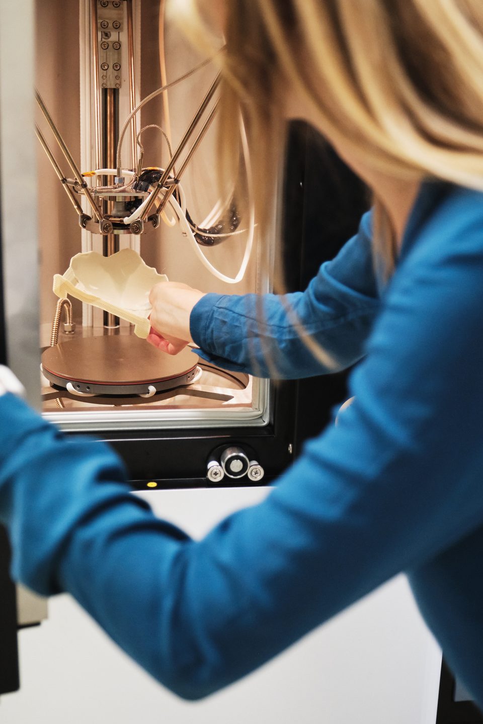 Nahaufnahme: ihre Hände arbeiten im Bauraum des 3D-Druckers an einem frisch gedruckten Bauteil