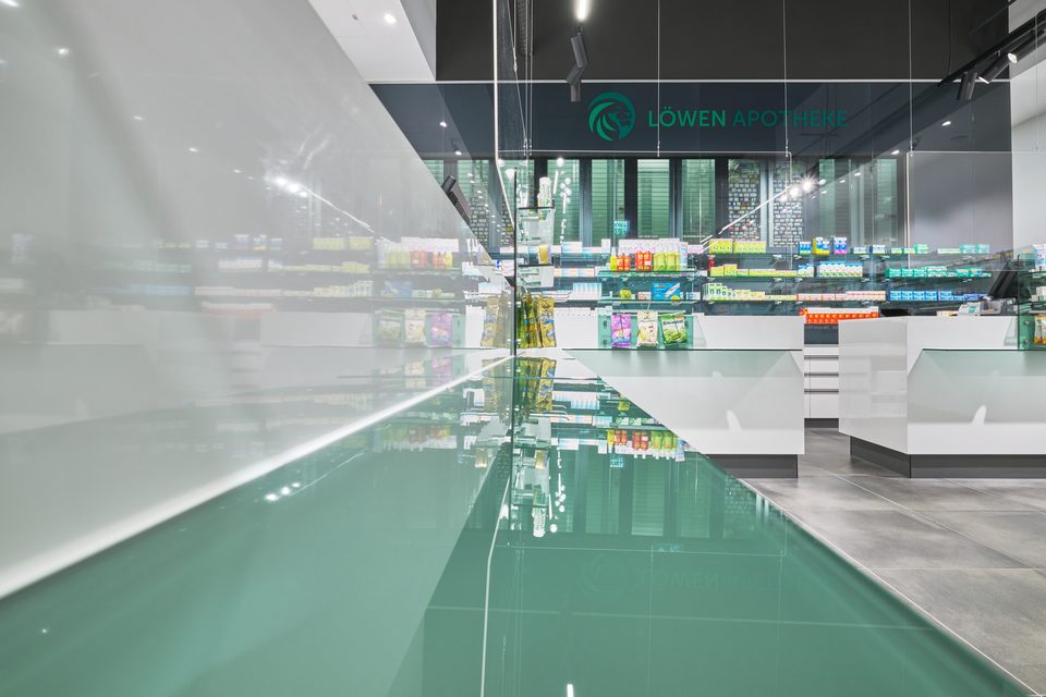 Mintgrüner Hochglanztresen der Löwen-Apotheke Melk, im Boden spiegelt sich das Logo an der dunklen Glaswand