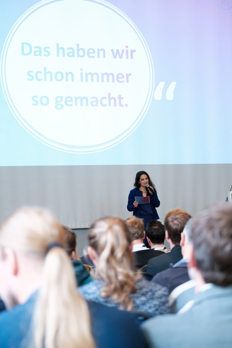 Auf der Leinwand das Zitat „Das haben wir schon immer so gemacht.", davor die Rednerin und das Publikum.
