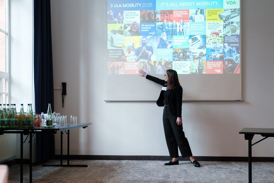 Referentin zeigt auf eine Projektion mit Motiven der IAA Mobility 2025.