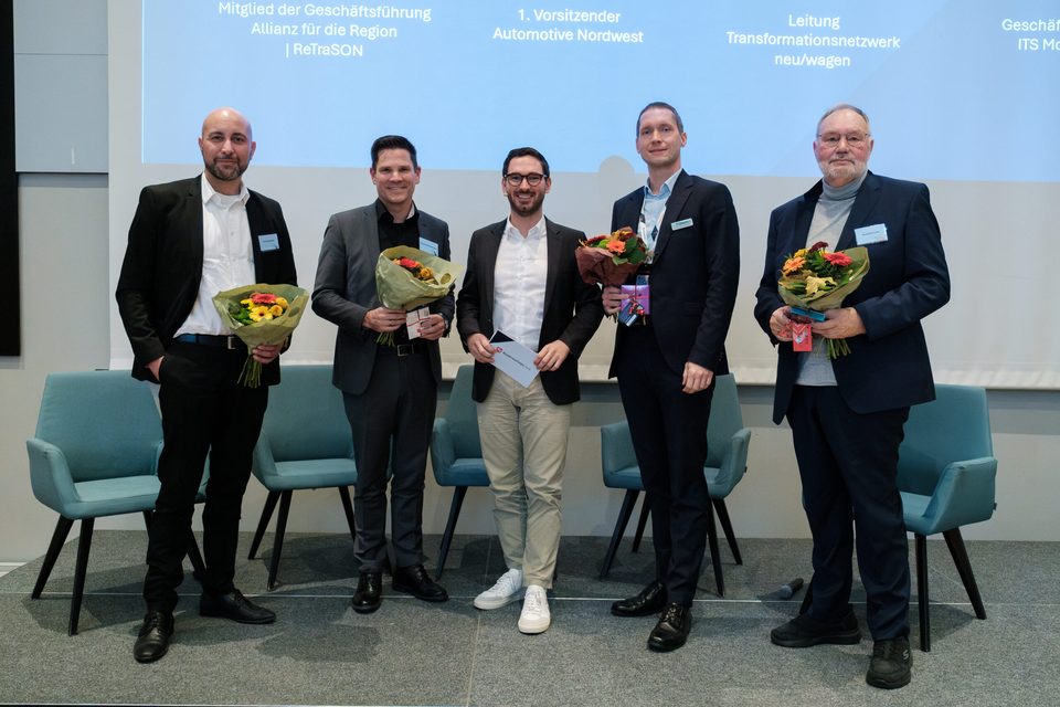 Fünf Podiumsgäste stehen mit Blumensträußen zum Abschluss vor der Leinwand mit ihren Funktionen.