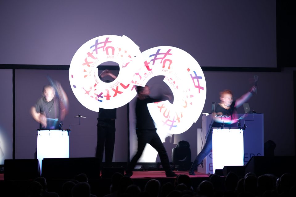 Lichtkunst-Showact auf der Bühne: zwei Performer zeichnen in Langzeitbelichtung einen leuchtenden Ring aus Hashtags in die Luft.