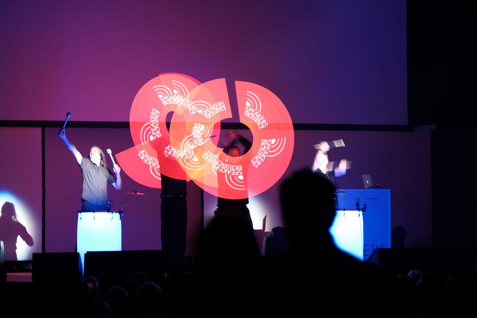 Rot leuchtende Lichtfigur entsteht während der Show, ein Performer reißt die Arme hoch.