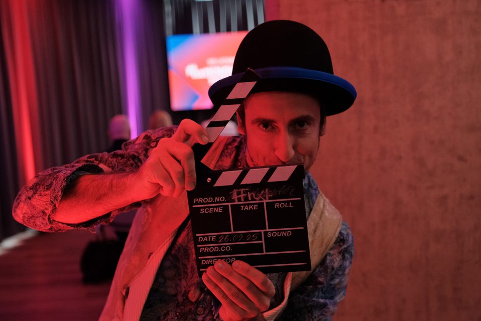 Künstler mit Melone hält eine Filmklappe vor sein Gesicht, rotes Bühnenlicht der Kongresshalle Böblingen.