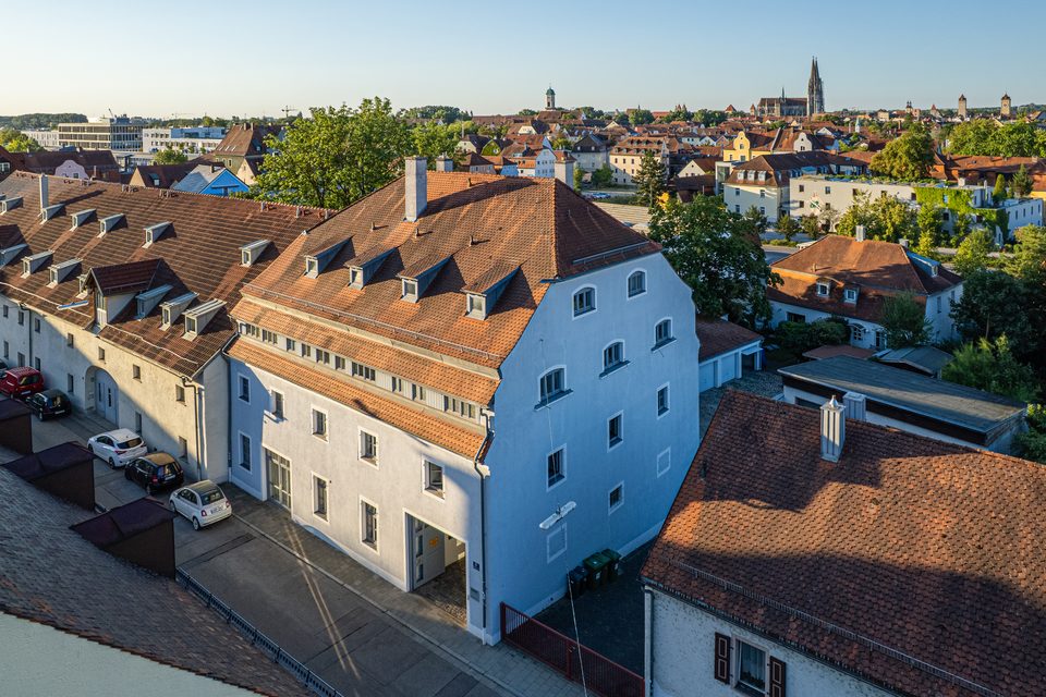 Erhöhte Außenansicht des Peppel-Dental-Labors mit Fassade im Morgenlicht, rotem Ziegeldach und Domtürmen in Regensburg
