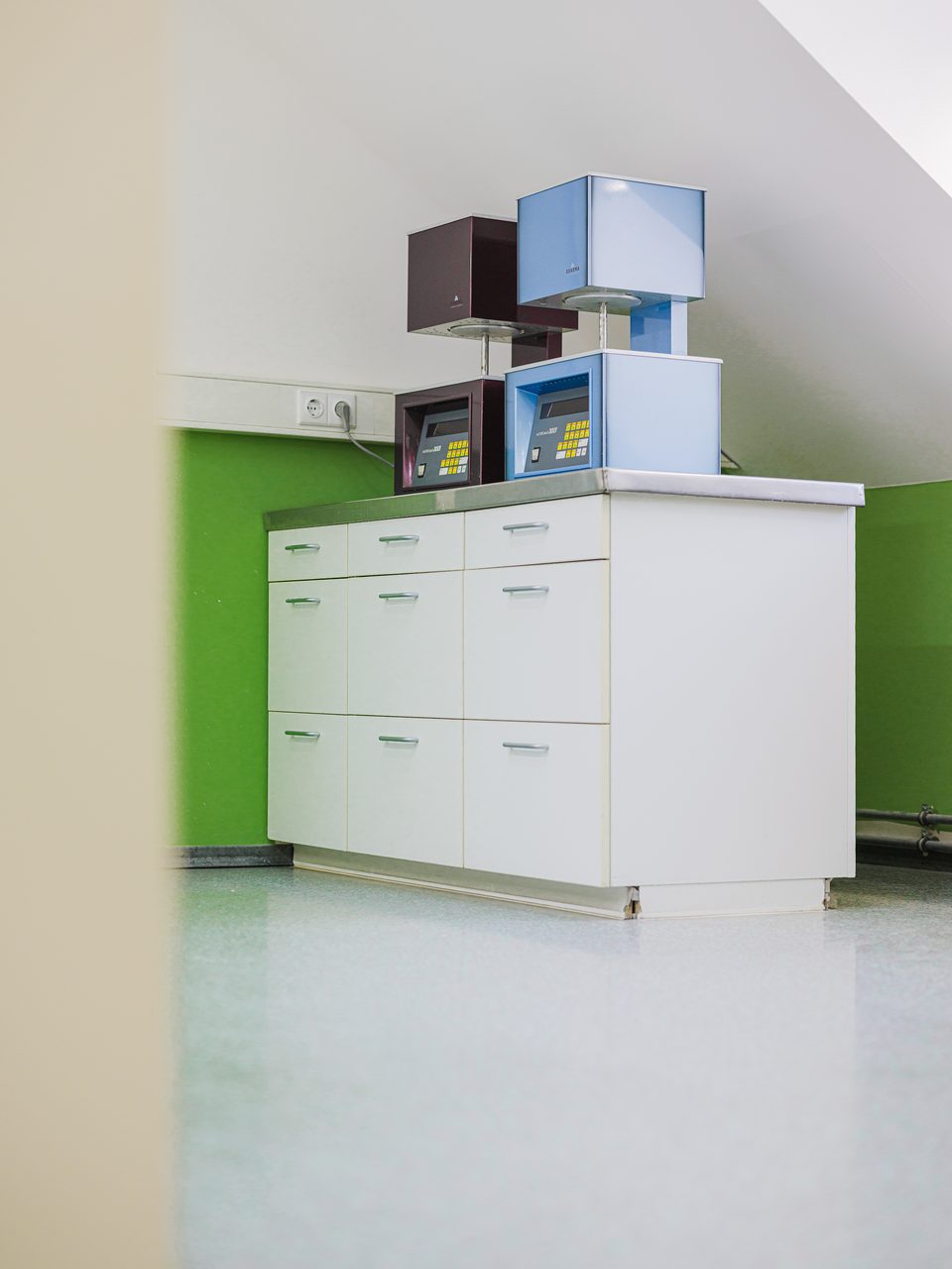 Hohe weiße Laborschränke vor der zweigeteilten Wand in Weiß und Apfelgrün
