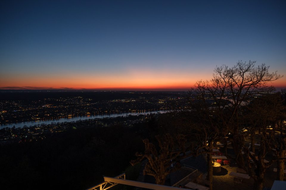 Das Abendrot glüht über der nächtlichen Landschaft, gesehen vom Balkon des Bankettsaals, mit dem Rhein und den funkelnden Lichtern der Bebauung
