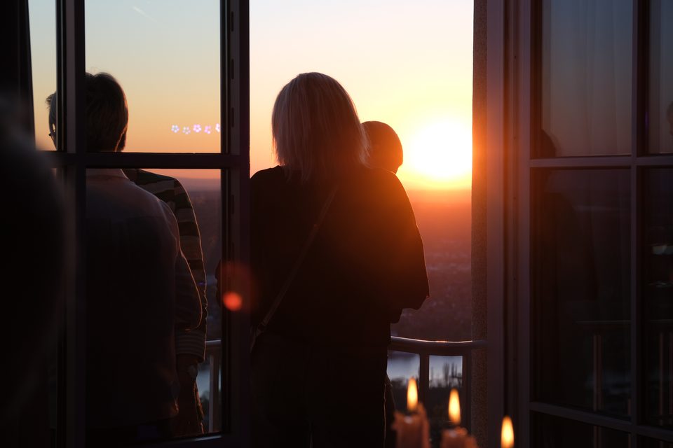Mehrere Menschen auf dem Balkon des Bankettsaals reden im Licht der Abendsonne, die fast den Horizont berührt