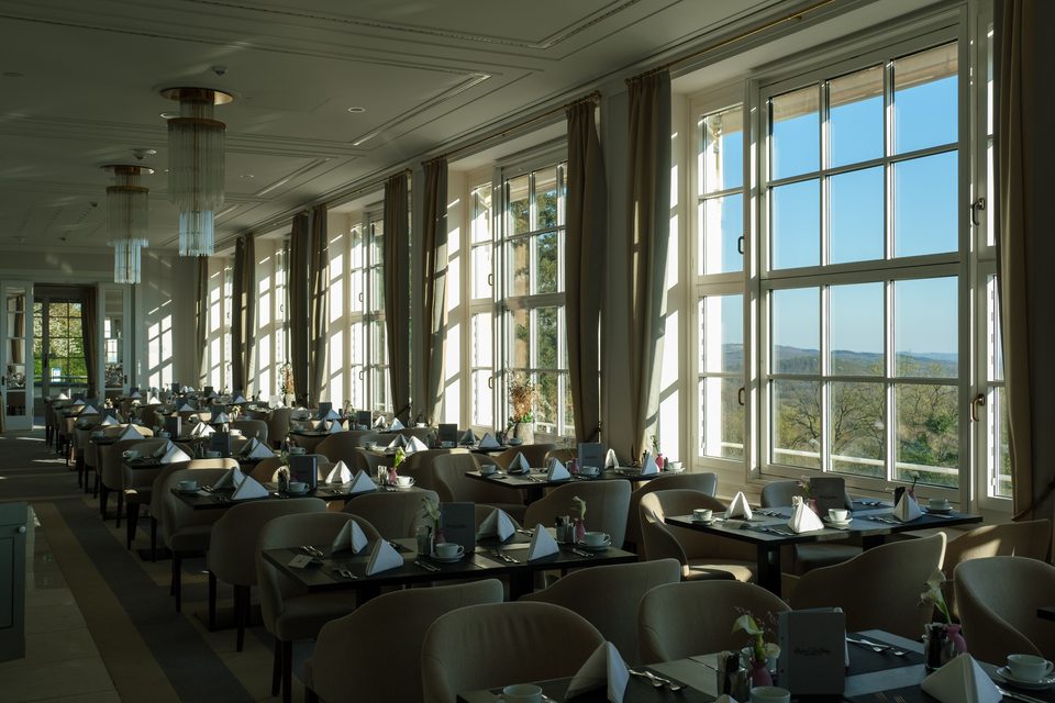 Blick in den leeren, aber eingedeckten Speisesaal mit langer Fensterfront und Aussicht in die Weite