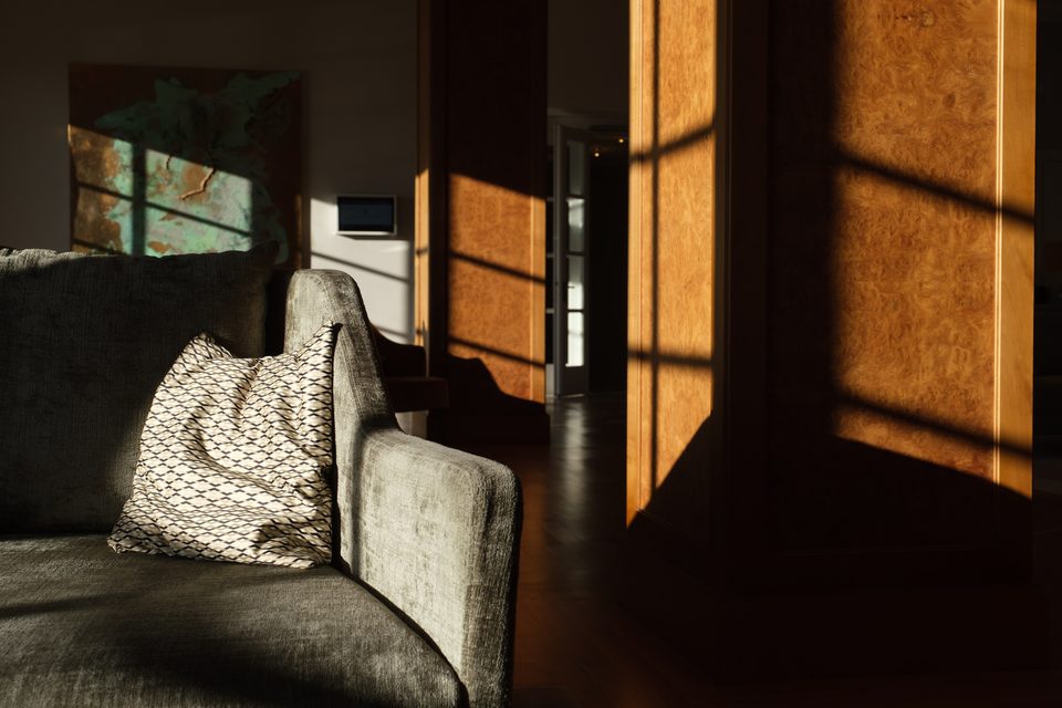 Loungeecke mit Sofa und gemustertem Kissen, auf der Wand zeichnet die Abendsonne das Muster der Fenster nach