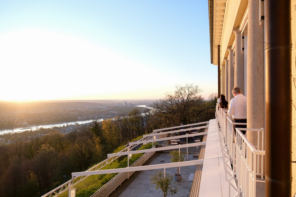 Blick von der Balustrade des Grandhotels entlang der Fassade ins gegenlichtdurchflutete Rheintal, zwei Gäste stehen an der Brüstung