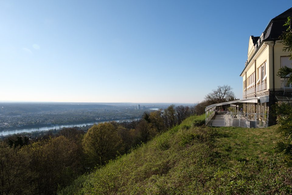 Das Steigenberger Grandhotel auf dem Petersberg über dem Rheintal, davor der bewaldete Hang und der Blick bis nach Bonn