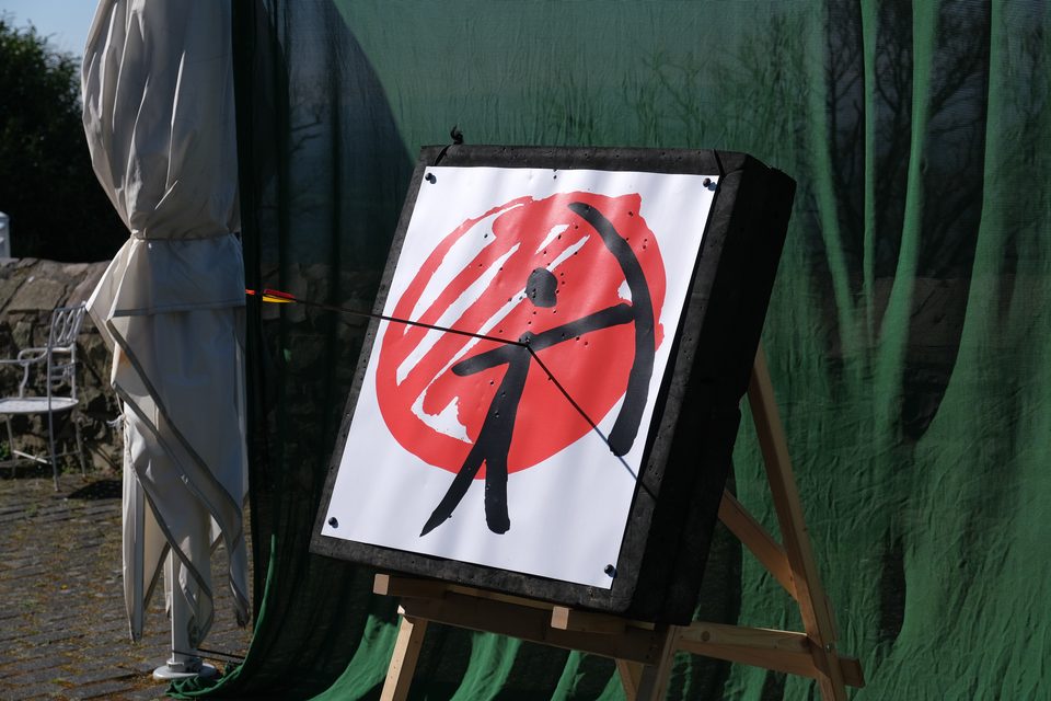 Zielscheibe mit dem roten Bogenschützen-Logo vor einem grünen Fangnetz auf der Terrasse