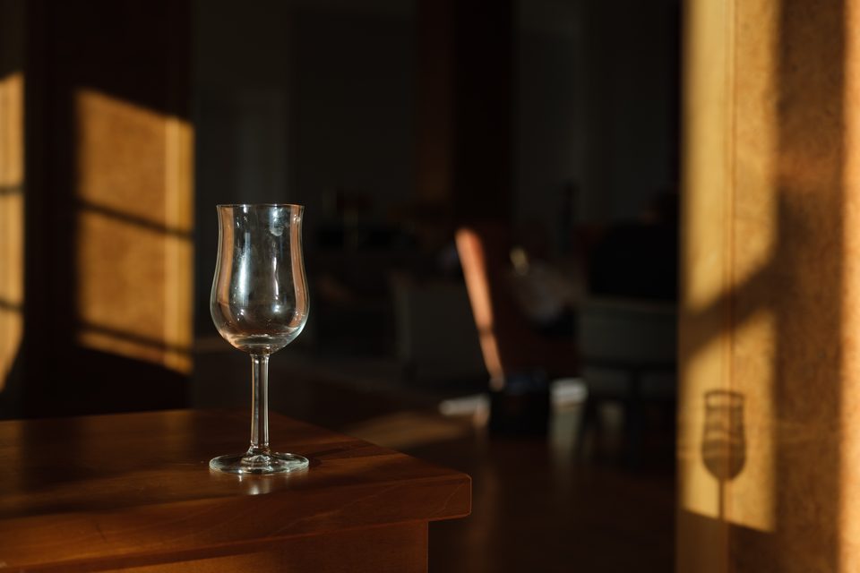 Leeres Stielglas auf einem Holztisch, dahinter die im Streiflicht liegende Lounge
