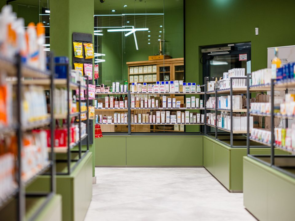 Blick zwischen den Warenträgern hindurch zur Sichtwahl, im Hintergrund der antike Apothekerschrank