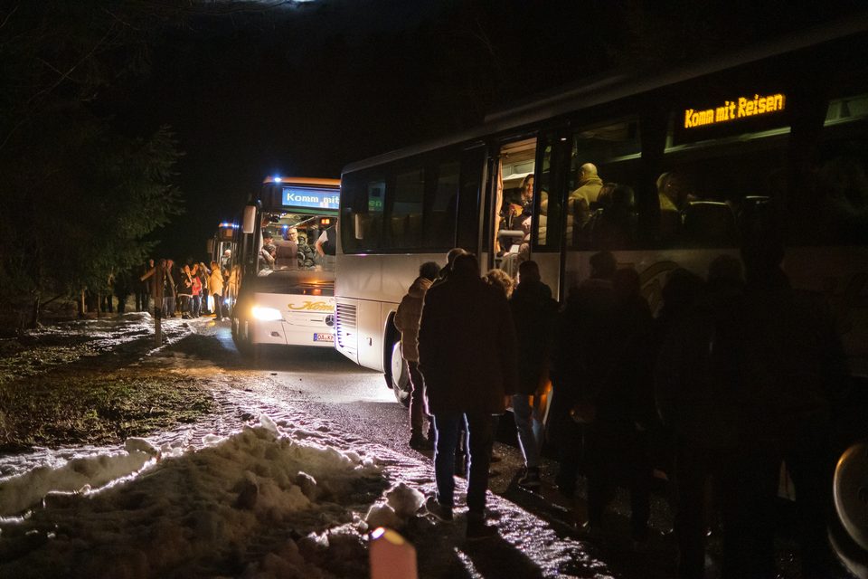 Drei Reisebusse entladen Teilnehmer für eine Abendveranstaltung am nächtlichen Straßenrand